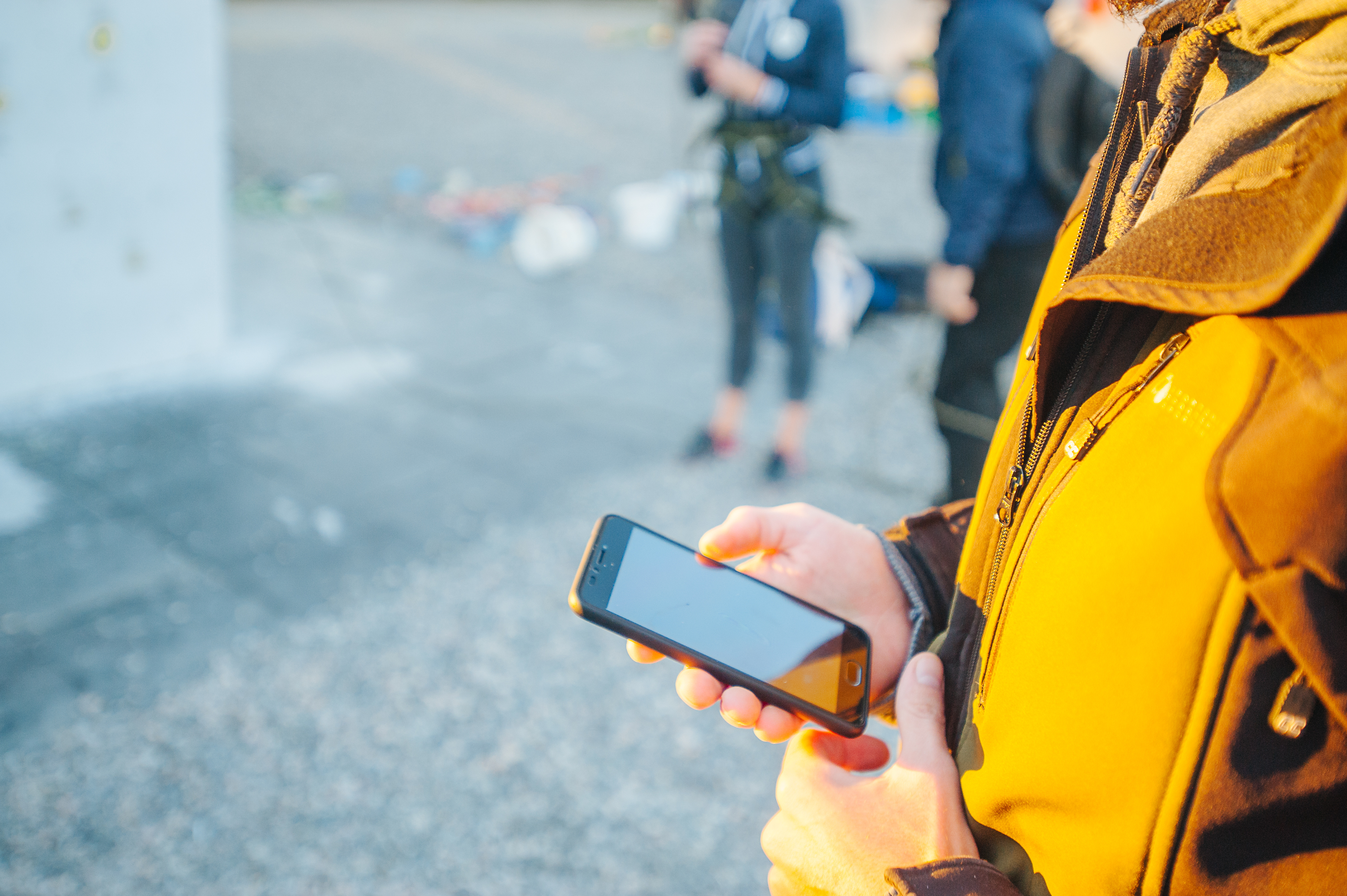 Man in yellow and black jacket hoding a mobile device